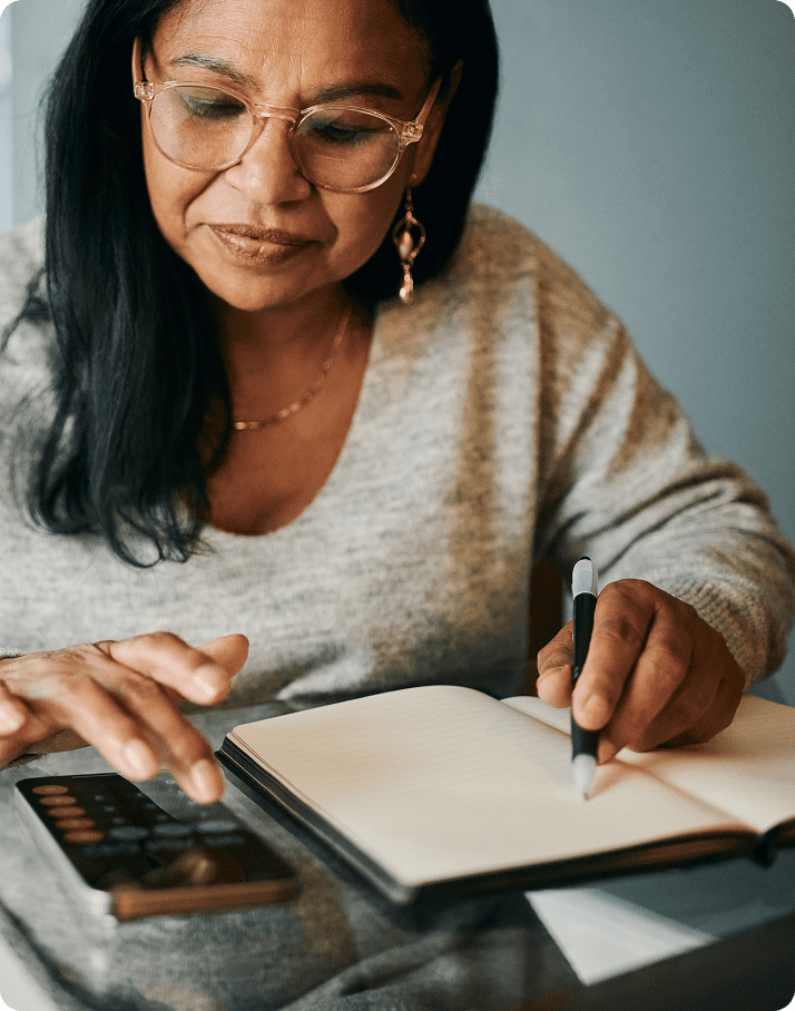 Woman writing in notebook, using smartphone.