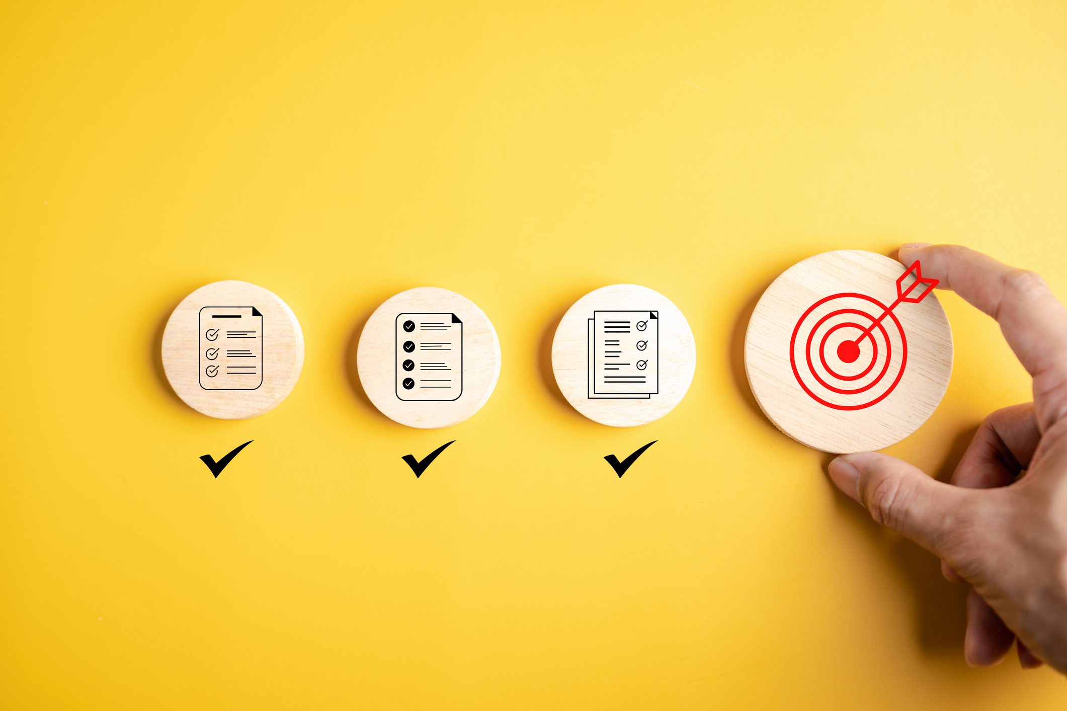 Goal planning and task completion strategy concept. Hand holding target icon after completing all checklist. Wooden blocks on yellow background progress to success.