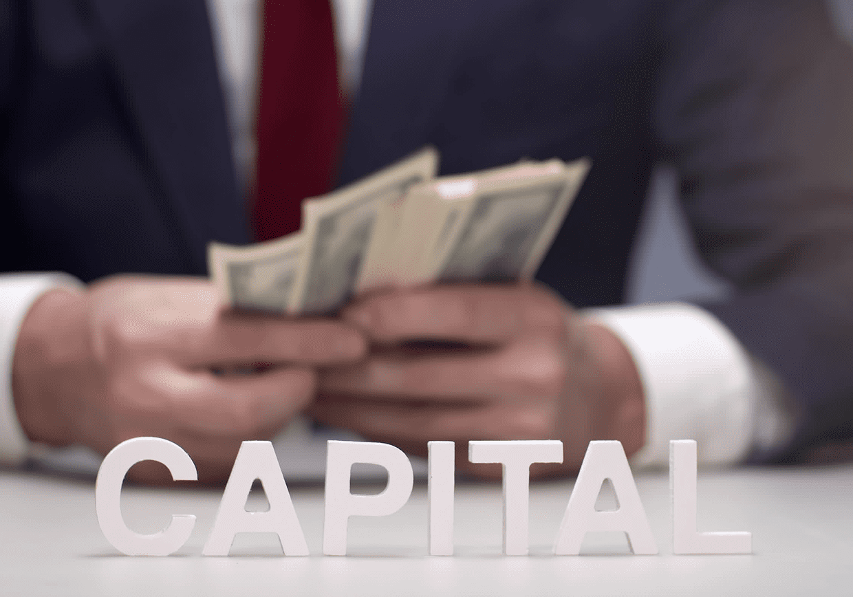 Man counting money behind "CAPITAL" letters.